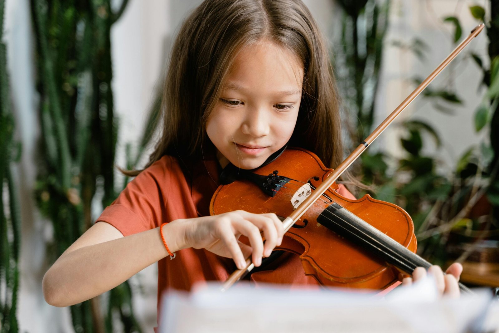 A young girl playing the violin with concentration in an indoor setting.